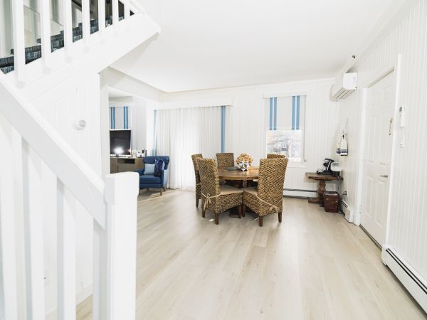 A bright, neatly furnished room with a dining table, four chairs, a blue couch in the background, and white walls with vertical blue-striped windows.