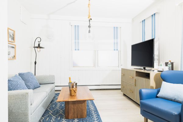 A cozy living room with a sofa, armchair, TV, and coffee table on a blue rug, decorated in a light, modern style.