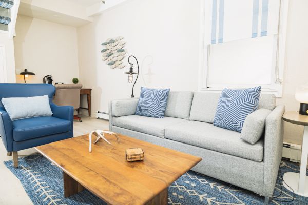 A modern living room with a gray sofa, blue armchair, wooden coffee table, and wall art. Blue and white accents adorn the space, with good lighting.