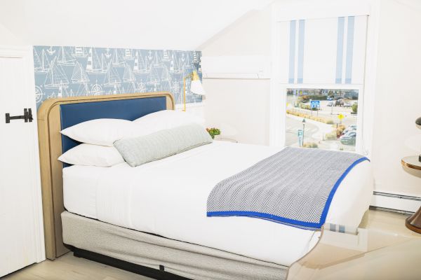 The image shows a tidy bedroom with a neatly made bed, blue and white décor, and a window overlooking an outdoor scene, ending the sentence.