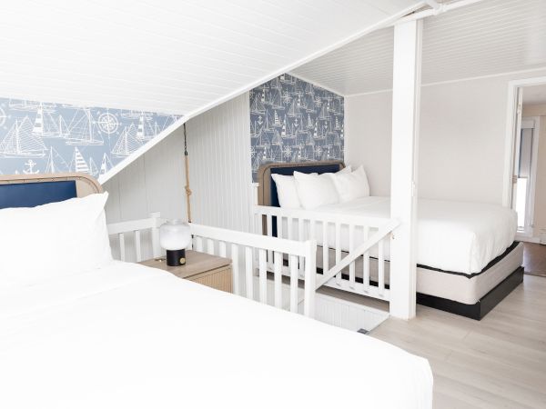 A bright nautical-themed bedroom with white bunk beds, crisp linens, and a compass sailboat wallpaper accent wall.