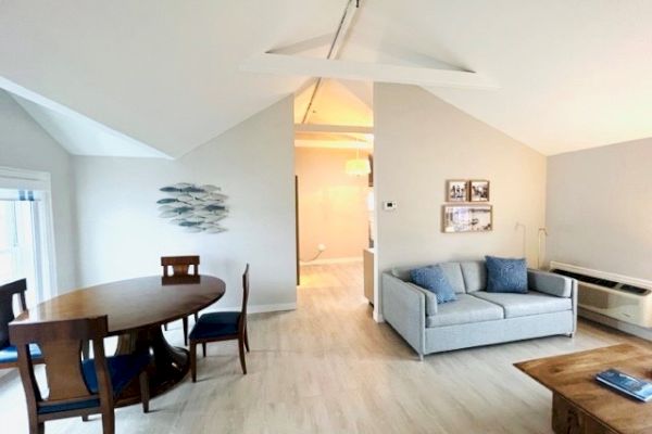 A modern living room with a round dining table, blue cushioned chairs, a gray sofa, wall art, and a coffee table in a well-lit space.