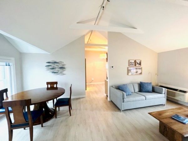 A modern living room with a round dining table, blue cushioned chairs, a gray sofa, wall art, and a coffee table in a well-lit space.