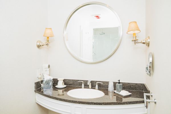 A modern bathroom vanity with a round mirror, two wall-mounted lights, a sink, a soap dispenser, and a tissue box on a granite countertop.