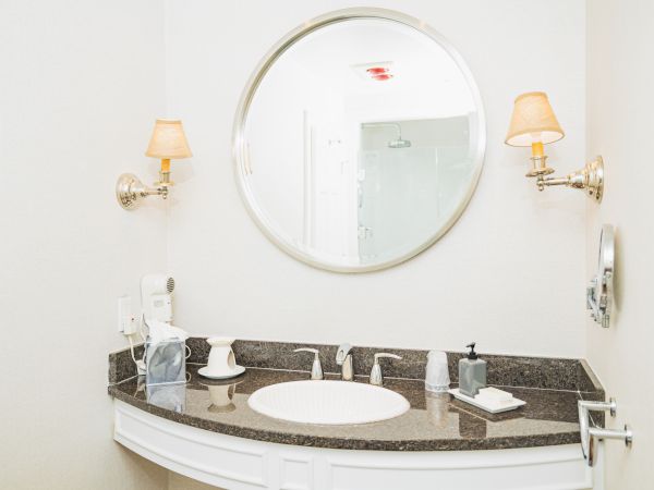 A modern bathroom vanity with a round mirror, two wall-mounted lights, a sink, a soap dispenser, and a tissue box on a granite countertop.
