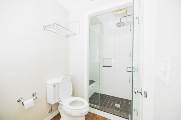 A minimalistic bathroom featuring a toilet, a stand-up shower, a towel rack, and a toilet paper holder.