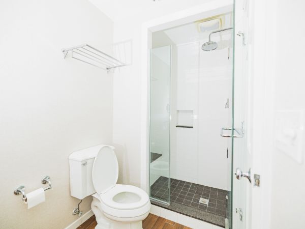 A minimalistic bathroom featuring a toilet, a stand-up shower, a towel rack, and a toilet paper holder.