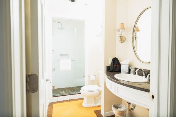 A clean bathroom with a glass shower, toilet, sink with a mirror, and a countertop with toiletries. A yellow mat is on the floor.