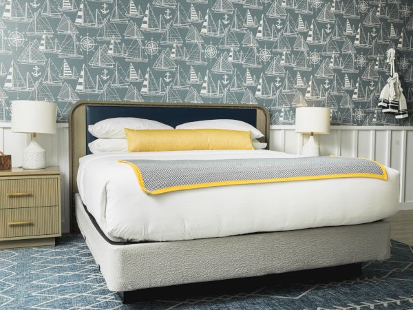 A neatly styled bedroom with a bed, two bedside tables, lamps, nautical-themed wallpaper, and a blue and white color scheme ending the sentence.