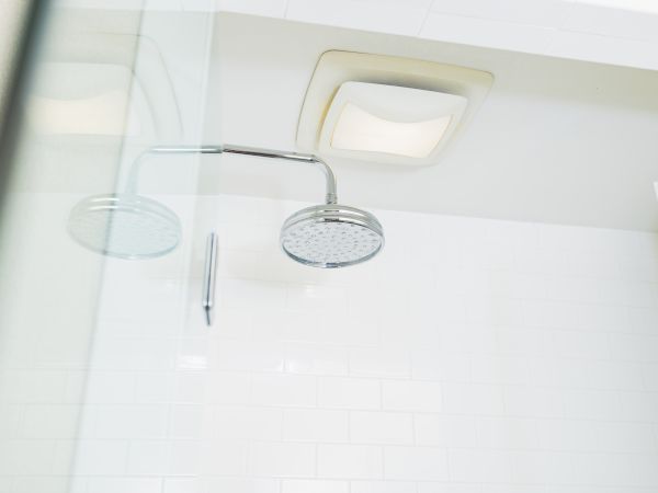 A modern shower area with a round showerhead, white tiled walls, and a ventilation fan on the ceiling.