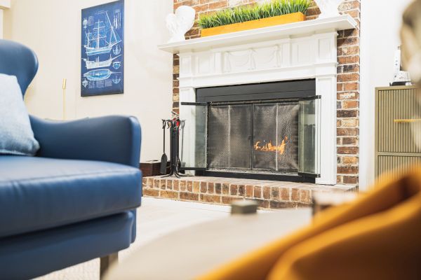 A cozy living room with a lit fireplace, blue armchair, wall art, and a touch of greenery on the mantel.