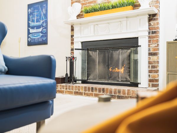 A cozy living room with a lit fireplace, blue armchair, wall art, and a touch of greenery on the mantel.