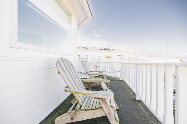 Two wooden chairs on a deck with white railings and a clear sky. The scene appears peaceful, ideal for relaxation.