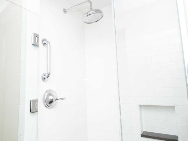 Chrome showerhead and faucet in a white tiled shower with clear glass panel.