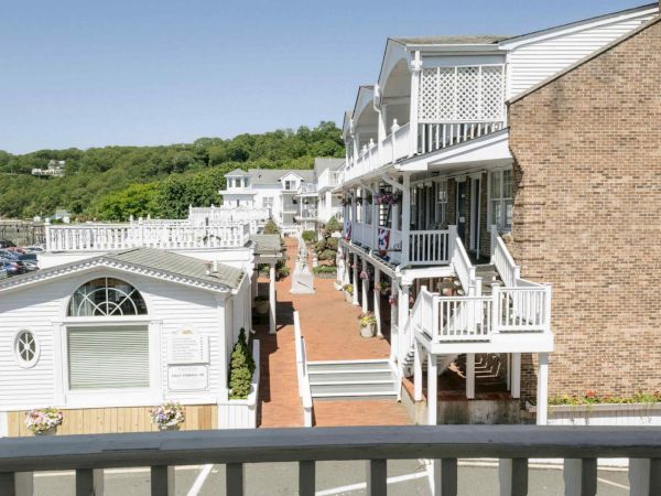 A long brick-and-white hotel balcony walkway with flower pots, stairs, and multiple levels overlooking trees and parked cars.