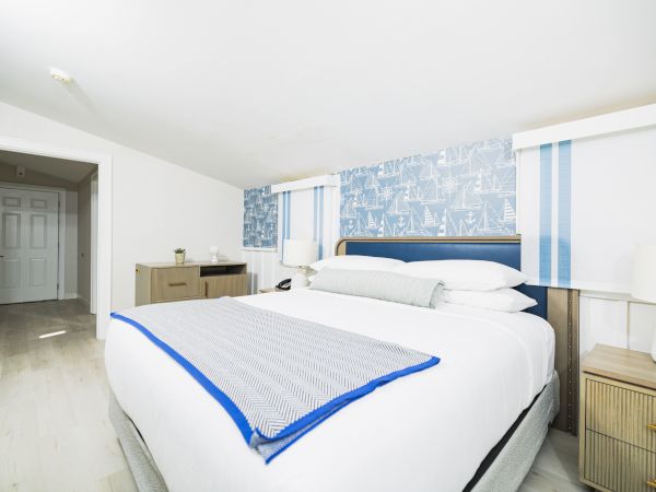 The image shows a modern bedroom with a large bed, blue and white bedding, nightstands with lamps, and a patterned blue accent wall.