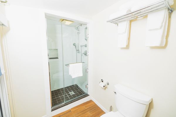 The image shows a bathroom with a shower enclosure, toilet, and towel rack holding folded towels and a washcloth above the toilet.