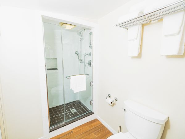 The image shows a bathroom with a shower enclosure, toilet, and towel rack holding folded towels and a washcloth above the toilet.