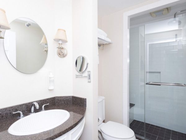 Modern bathroom: vanity sink with round mirror and wall lamps, plus a glass shower, tiled walls, and a toilet.