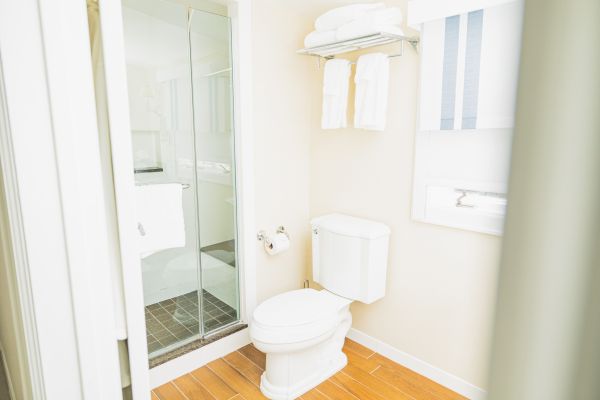 The image shows a bathroom with a shower, a toilet, a towel rack holding neatly folded towels, and a toilet paper holder.