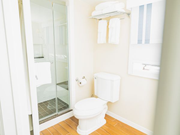 The image shows a bathroom with a shower, a toilet, a towel rack holding neatly folded towels, and a toilet paper holder.