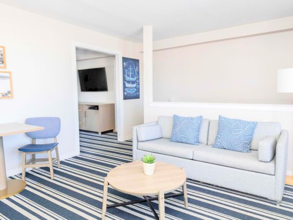 Bright living room with a gray sofa, blue patterned pillows, striped rug, coffee table, and a small round bistro set.
