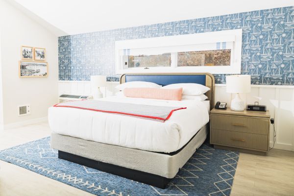 A bright, modern bedroom with a double bed, blue patterned accent wall, bedside tables, lamps, and a blue rug, decorated in a nautical theme.