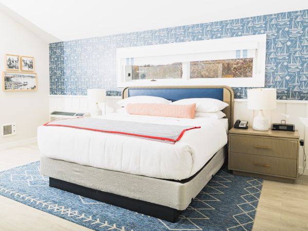 A bright, modern bedroom with a double bed, blue patterned accent wall, bedside tables, lamps, and a blue rug, decorated in a nautical theme.