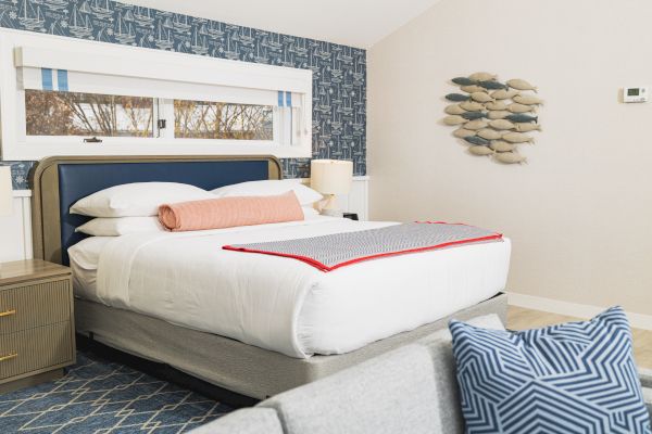 A neatly made bed with white bedding, pink and gray accents, a wooden nightstand, and fish wall decor in a modern bedroom setting.