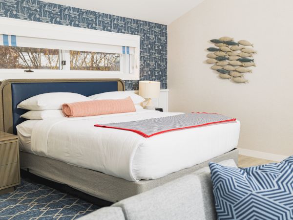 A neatly made bed with white bedding, pink and gray accents, a wooden nightstand, and fish wall decor in a modern bedroom setting.