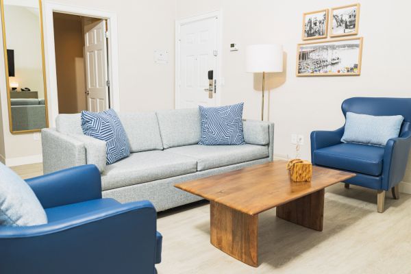 A modern living room with a gray sofa, blue armchairs, wooden coffee table, wall pictures, and a floor lamp in a minimalist setting.