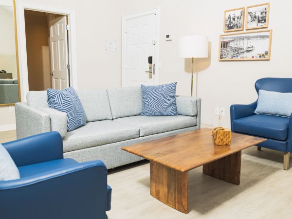 A modern living room with a gray sofa, blue armchairs, wooden coffee table, wall pictures, and a floor lamp in a minimalist setting.