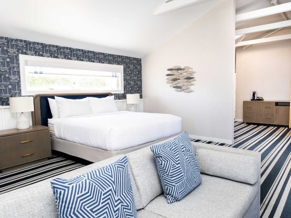 Bright nautical-themed bedroom with a bed, navy sailboat wallpaper, striped rug, and fish wall art.