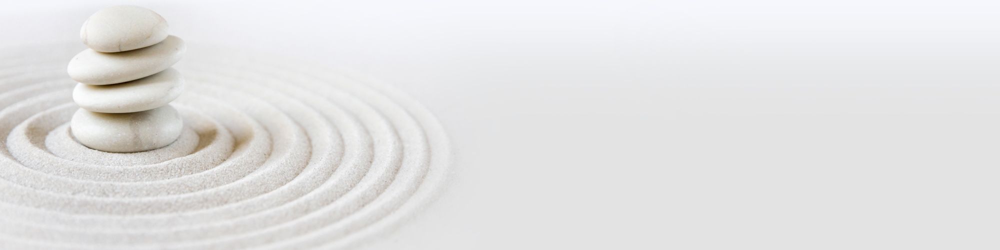 A stack of smooth white stones on raked sand with concentric circles, creating a minimalist and zen-like scene.