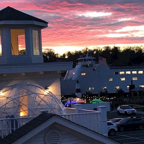 Sunset glow over a white building with a cupola, dome greenhouse, and string lights on a quaint harbor town at dusk.