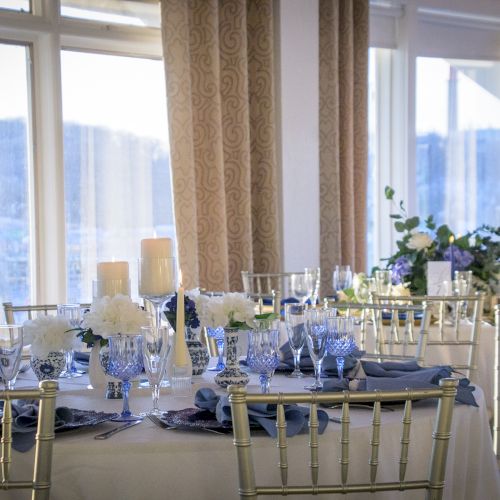 A bright dining hall with long tables set for a meal, large windows, warm light, and blue chairs&mdash;looks ready for a formal gathering.