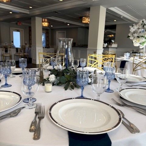A formal dining room with round tables, blue chairs, white plates, and a buffet/servers in the background, ready for guests to dine.