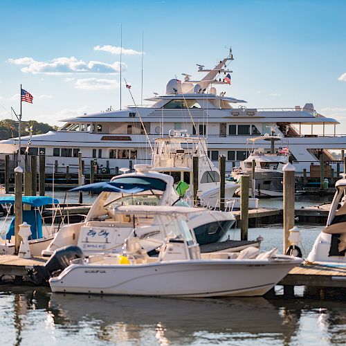 A marina filled with various boats and yachts, with a large luxury yacht in the background on a sunny day.