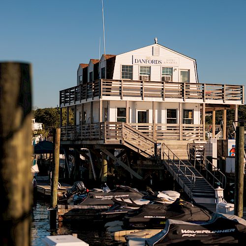 A waterfront building with a sign reading "Boat Rentals," docked boats, and jet skis in the foreground, set against a clear sky.