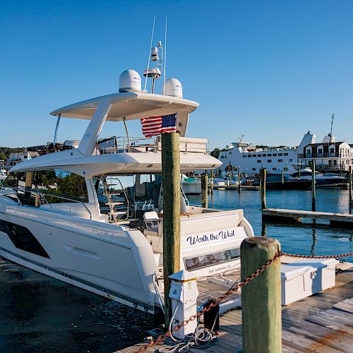 A luxury yacht docked at a marina with an American flag, surrounded by several other boats and a clear blue sky, is seen in the image.