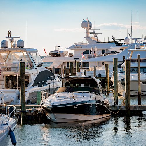 The image shows a marina filled with several yachts and boats docked in the water under a clear sky.