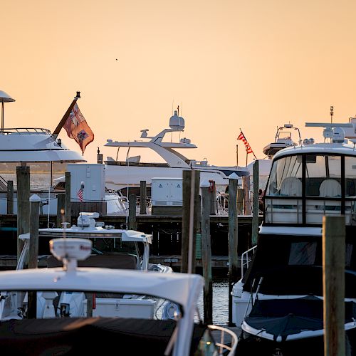 Several yachts docked at a marina during sunset, with their masts and flags in view, creating a peaceful nautical scene.