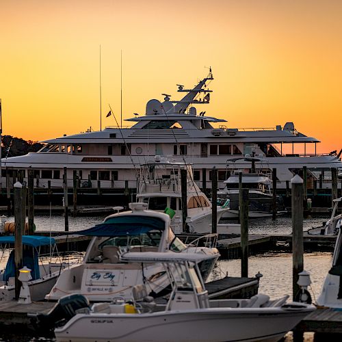 The image shows a marina with several boats and yachts docked at sunset, under a vibrant orange sky.