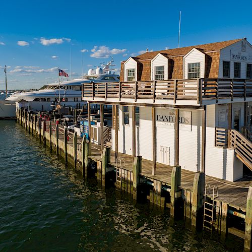 A waterside building with "Donald's" on it, docked yachts, and a calm sea under a clear blue sky, surrounded by wooden barriers.