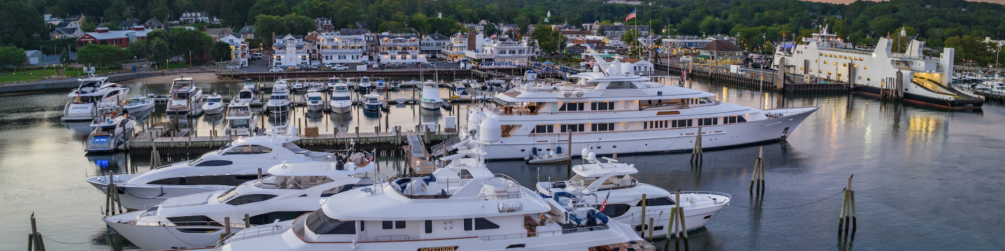 The image shows a marina filled with docks and yachts bathed in a warm sunset glow, with buildings and trees in the background filling the horizon.