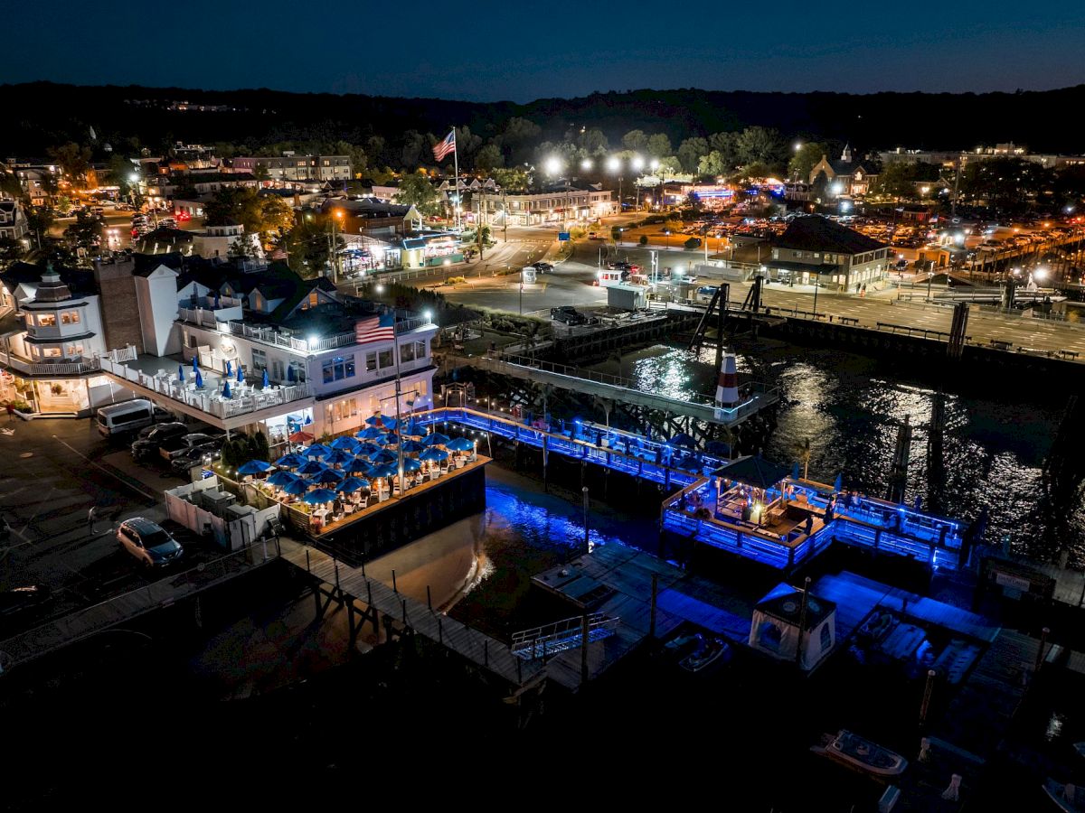 The image depicts a vibrant waterfront area at night, with illuminated buildings, piers, and reflections on the water.