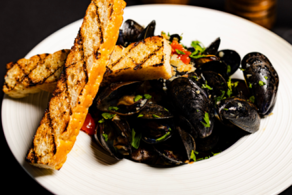 A dish of mussels garnished with herbs and diced tomatoes, served with two pieces of grilled bread on a white plate.