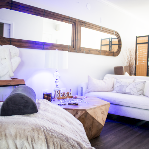 A cozy living room with a white sofa, throw pillows, modern wooden coffee table, large wall mirror and decorative elements including a small statue.