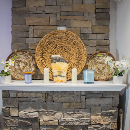 The image shows a decorated stone fireplace mantel featuring woven baskets, candles, plants, and a large crystal, creating a cozy atmosphere.