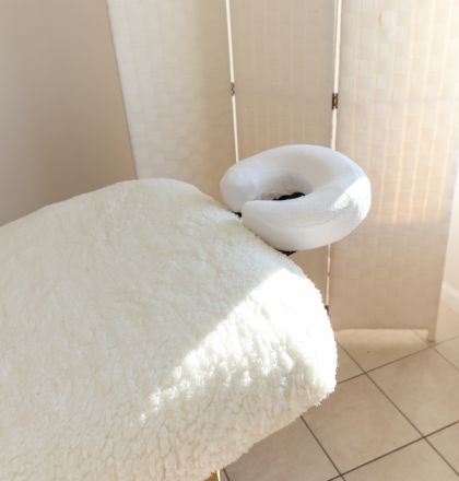 The image shows a massage table with a soft, white covering and a face cradle, placed in a room with a tiled floor and a privacy screen.